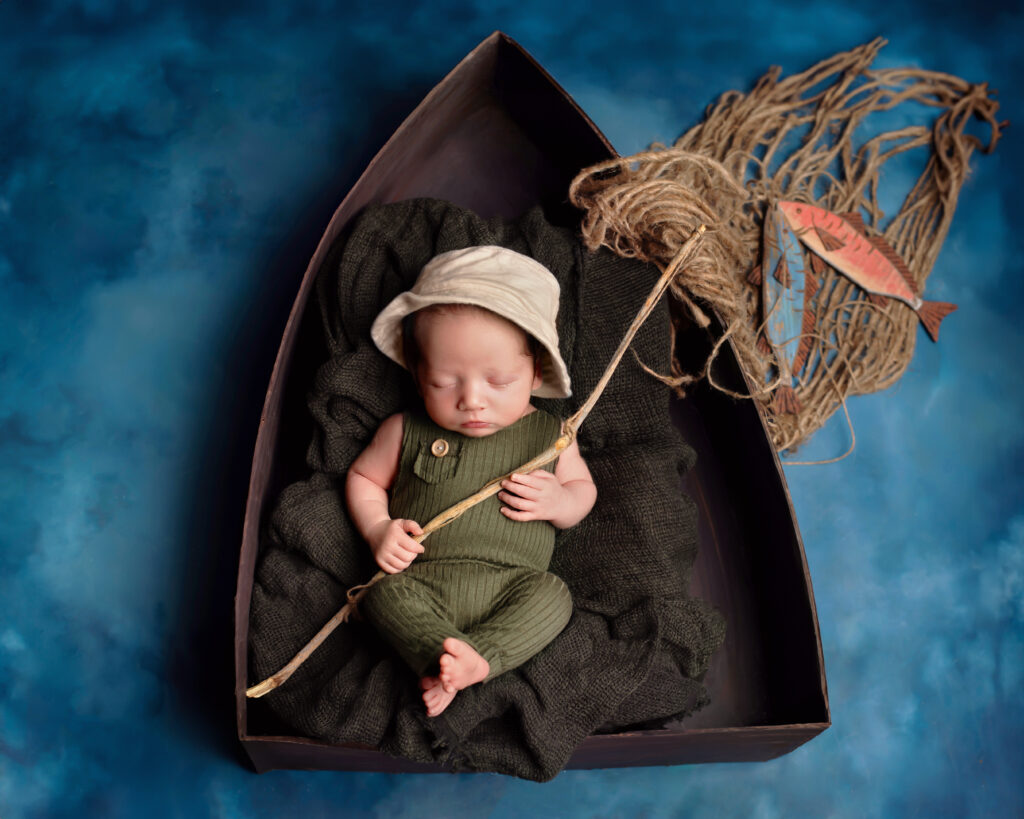 beautiful baby boy in a fishing photoshoot lying in a boat prop with fish in Eagle Mountain Utah